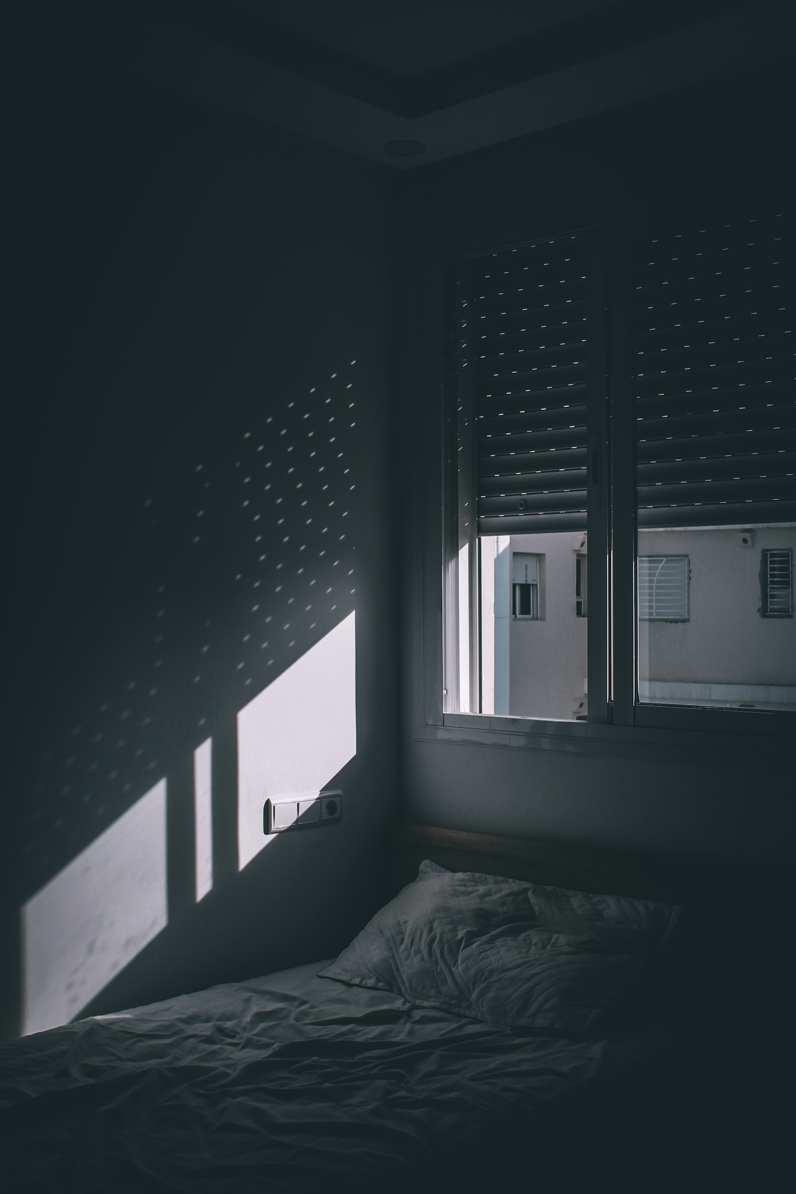 A darkened room with daylight cutting through closed blinds